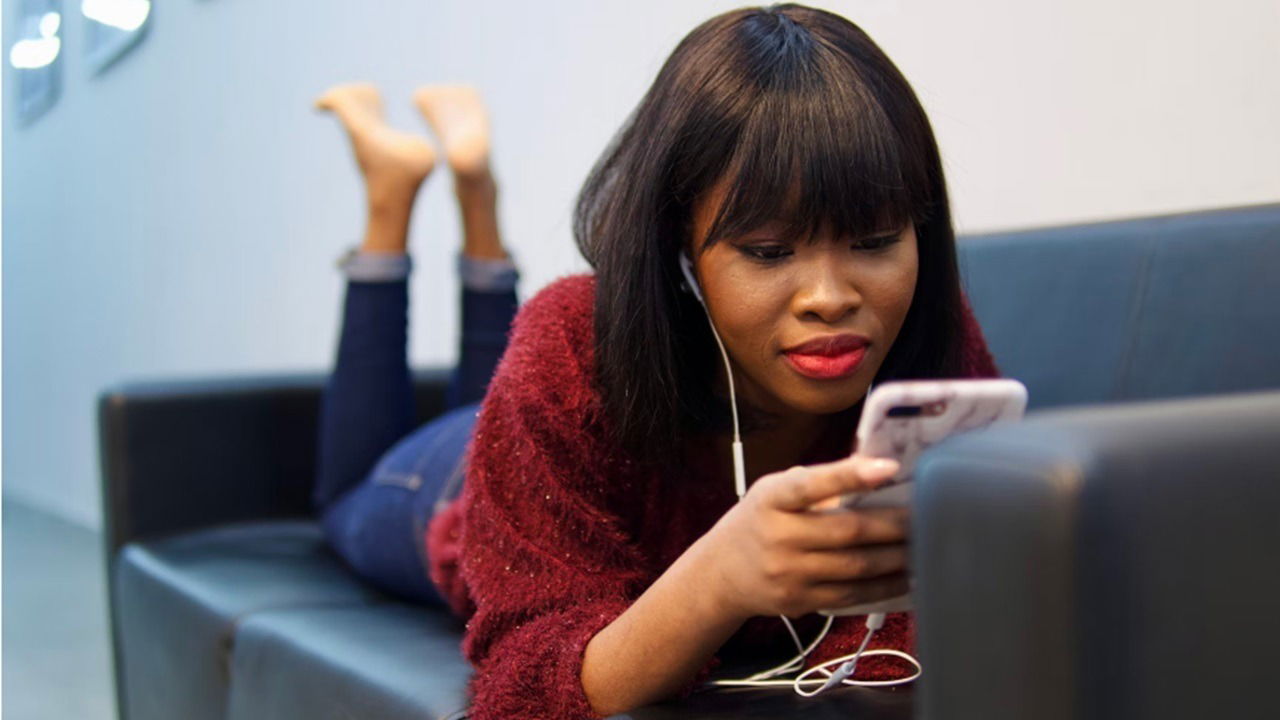 Woman laying on couch watching videos on her phone.