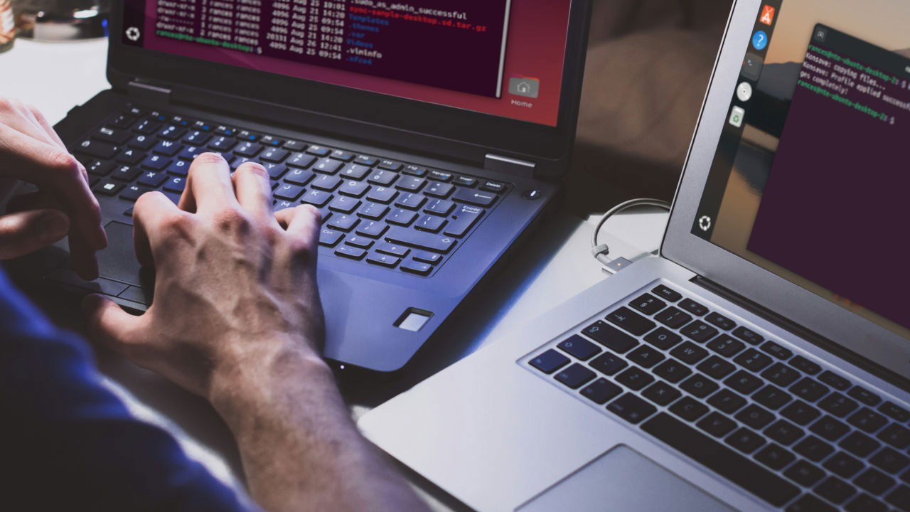 A photograph showing a person working on two different laptops.