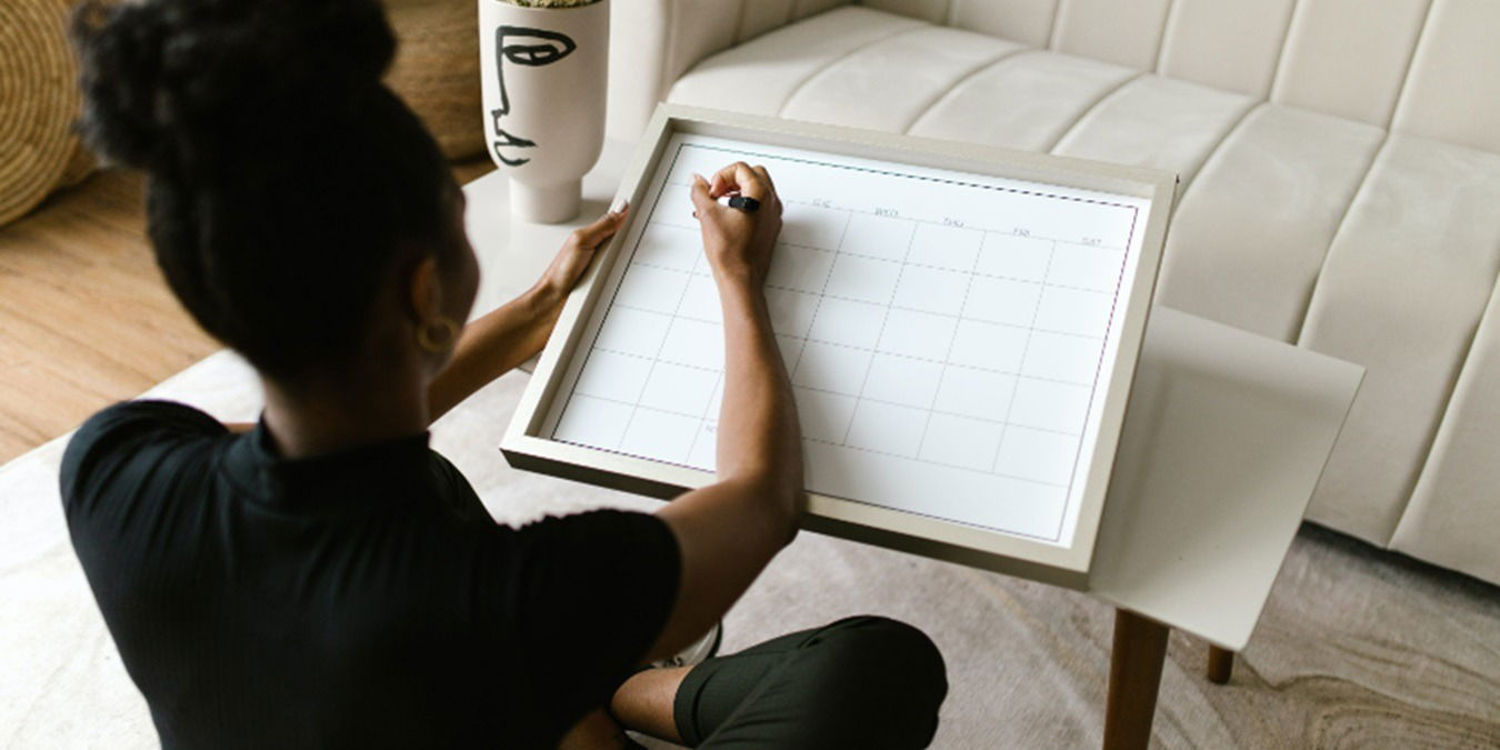 Woman sitting in the floor writing on a wall calendar.