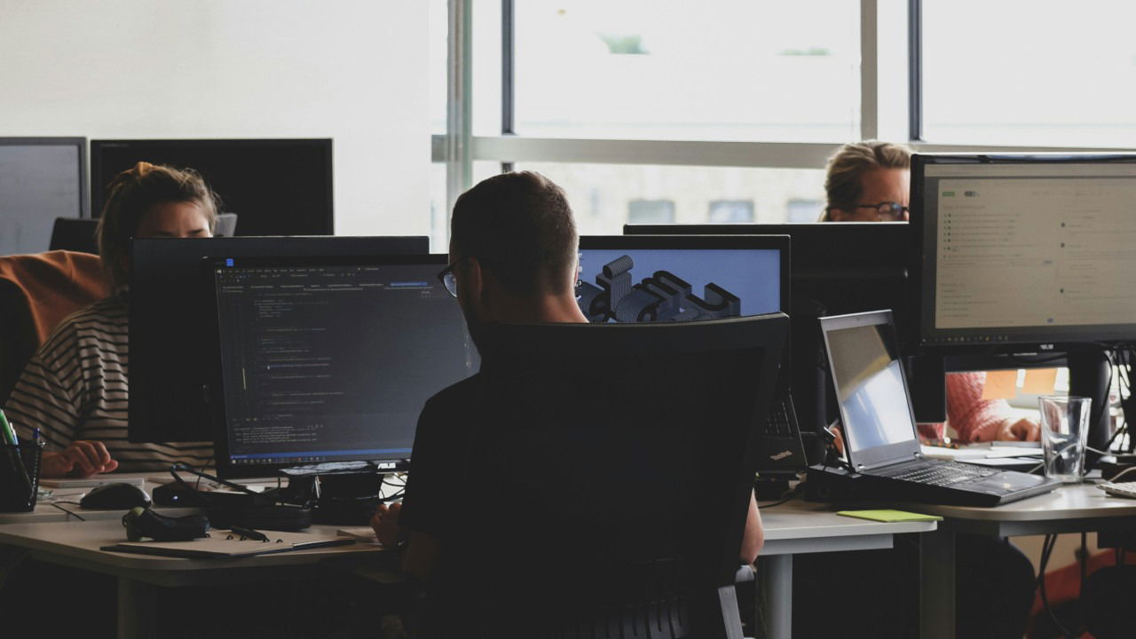 A photograph of an office space with people working on their computers.